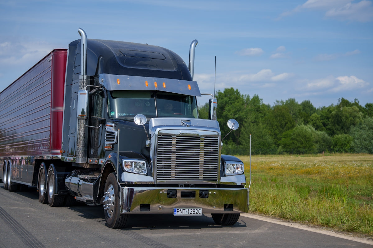 A black semi-truck drives down a rural road.